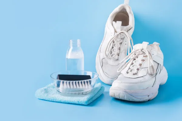a-pair-of-dirty-white-sneakers-with-cleaning-supplies2c-including-a-brush2c-cloth-and-soapy-water-against-a-blue-background Giày bánh mì cần được vệ sinh đúng cách bằng bọt chuyên dụng để duy trì vẻ đẹp và độ bền
